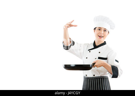 Gara di misto asiatico modello cinese tenendo un pan mostra chef sale di irrorazione in aria e aggiungendo i gesti di stagionatura in piedi sul muro bianco sullo sfondo Foto Stock