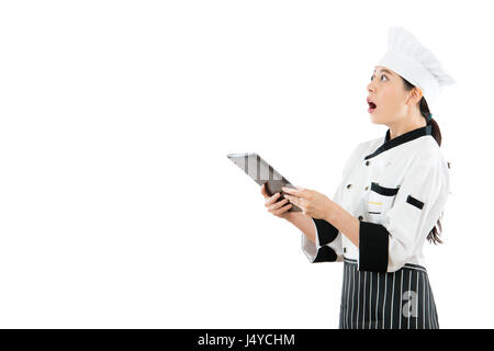 Bella chef sorpreso cercando copyspace vuoto permanente sulla parete bianca di sfondo e azienda moderna computer mobile pad nella ricerca di informazioni. Foto Stock