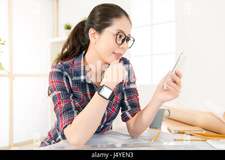 Professione e lavoro di concetto di occupazione. bella asiatica architetto donna felice per la lettura di messaggi di testo messaggio con tenendo lo smartphone e indossando smartwatch Foto Stock