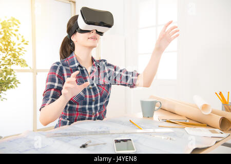 Efficiente razza mista asiatica femminile cinese architetto guardando il modello tramite VR nuova tecnologia mentre alla scrivania in ufficio creative studio. Foto Stock