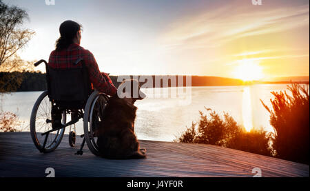 Donna in carrozzella con il suo cane al tramonto Foto Stock