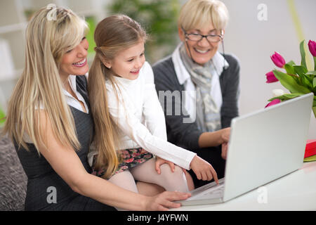 Ragazza carina la digitazione su laptop mentre mamma e nonna cercando che Foto Stock