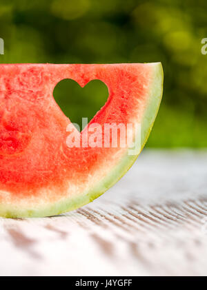 Fetta di anguria con un foro a forma di cuore su di un tavolo di legno Foto Stock