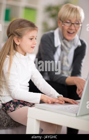 Adorabile bambina utilizzando laptop sorpreso nonna cercando Foto Stock