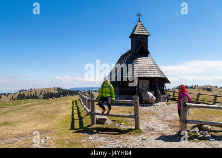 Sorridenti escursionisti in appoggio vicino alla piccola chiesa di montagna nella natura della montagna sulla giornata di sole, Velika planina, Slovenia, contro il luminoso cielo blu Foto Stock