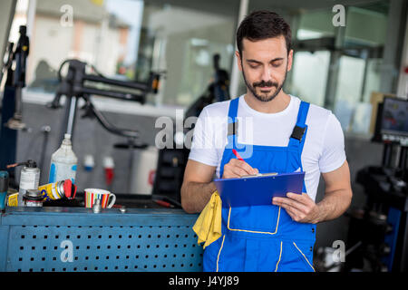 Meccanico nel negozio di riparazioni auto permanente e la scrittura su Appunti Foto Stock
