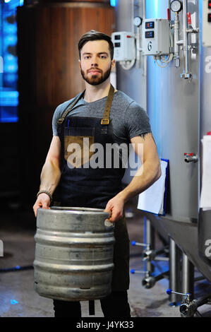 Birraio maschio con un metallo barile di birra sullo sfondo della birreria Foto Stock