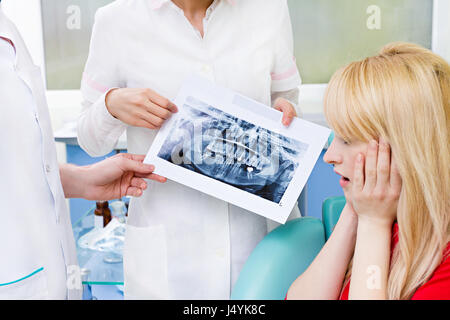 Closeup ritratto preoccupato spaventata paziente di sesso femminile, donna ubicazione in sedia ufficio medico, guardando dentali panoramica di immagini a raggi x di ascolto medico givi Foto Stock