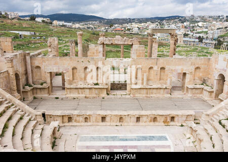 Teatro romano a Jerash, Giordania con vista della città dietro la fase i e cielo nuvoloso sopra. Il pavimento della sala teatro dispone di un pavimento a mosaico. Foto Stock