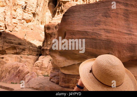 Donna che indossa un cappello di paglia, guardando le colorate in arenaria Al-Siq, Petra Giordania. La donna il cui hat corrisponde la pietra si trova in basso a destra. Foto Stock