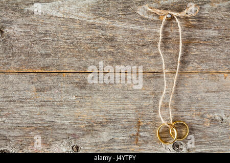 Oro due anelli di nozze legato con una corda appesa sulla parete in legno Foto Stock