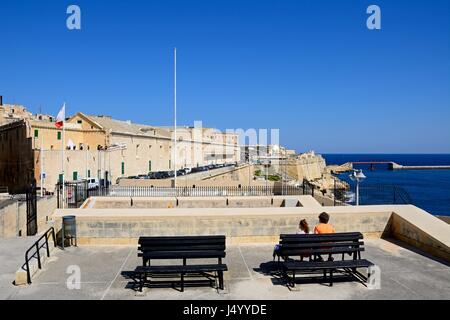 Vista dall'Assedio Memorial verso nord lungo Triq Il-Mediterran con una coppia seduta su una panchina guardando la vista in primo piano, La Valletta, Foto Stock