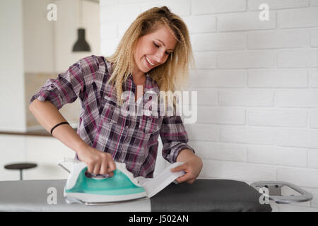 Bella giovane donna è la stiratura di panni a casa Foto Stock