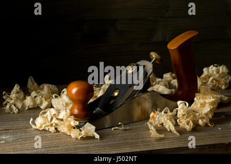 Macchine per la lavorazione del legno Pialla a mano attrezzo su assi di legno nella bottega del falegname contro il marrone scuro dello sfondo con spazio di copia Foto Stock