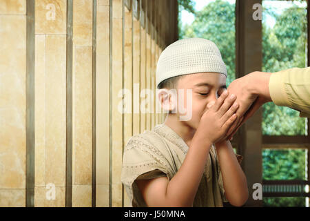 Musulmani asiatici kid baciare il suo genitore mano come simbolo di rispetto nella moschea Foto Stock