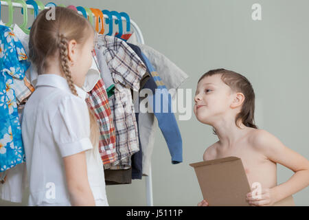 Due bambini piccoli in piedi vicino a un appendiabiti con vestiti di casa al giorno. I bambini divertendosi indoor. Foto Stock