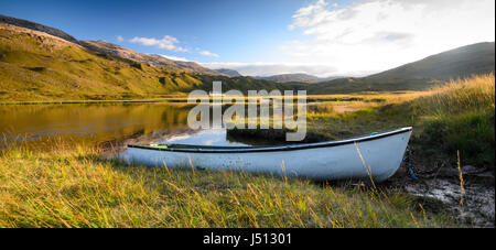 Una piccola barca a remi sulle rive del Lochan un lago Iasgair nel fondovalle di Glen Torridon, sotto le colline Torridon montagne di West Highl Foto Stock