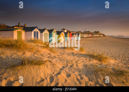 Dopo una fredda notte chiara, c'è una bellissima alba oltre la famosa linea di cabine sulla spiaggia, sulle dune a Suffolk cittadina balneare di Southwold. Foto Stock