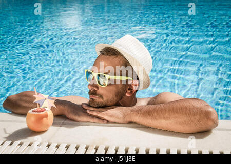 Giovane ragazzo appoggiata sul bordo piscina e godere della soleggiata giornata estiva Foto Stock