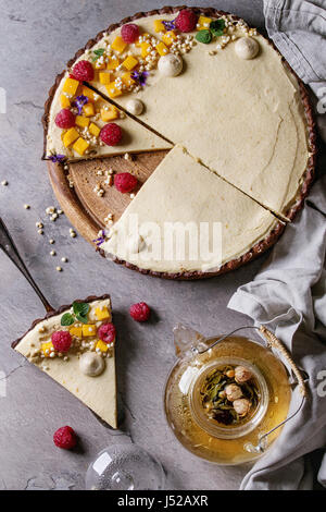 In casa fette di torta al cioccolato e pezzo di torta decorata da mango, lamponi, menta, il riso soffiato e fiori commestibili servita con vetro teiera su g Foto Stock