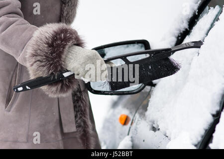 Mano di donna in mitten pulizia di un auto da neve con una spazzola Foto Stock