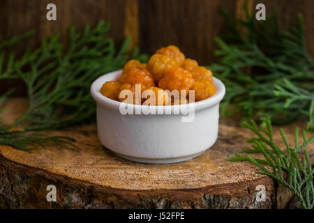 Decapati bacche di rovo in uno sciroppo zuccherino in una ciotola bianco sullo sfondo di legno con le foglie di ginepro Foto Stock