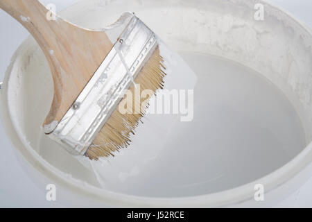 Un pennello di legno per immersione in un nuovo possibile di vernice bianca. Foto Stock