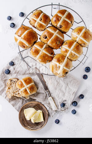 Hot cross panini sulla griglia da forno servita con burro, mirtilli freschi, il coltello e la brocca di crema su papkin tessili su bianco texture di sfondo di calcestruzzo. Foto Stock