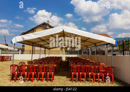 Intrattenimento bianco tenda rossa con sedie di plastica in giardino Foto Stock