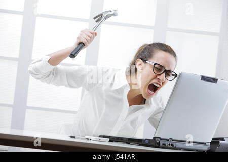 Freaked fuori imprenditrice con un martello pronti a distruggere il suo computer portatile Foto Stock