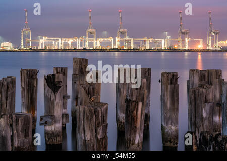 Vecchi tralicci da un molo, durante il tramonto, con un background industriale all'orizzonte Foto Stock