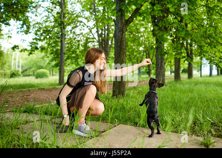 Una ragazza sta giocando con il suo cane bulldog francese nel parco. Foto Stock