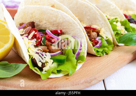 Tacos è un tradizionale piatto messicano. Tortilla farcita con pollo, Campana e peperoncino, fagioli, lattuga, formaggio, cipolla blu con salsa di salsa su bianco Foto Stock