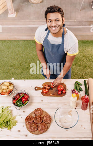 Uomo che fa gli hamburger e il taglio di pomodori rossi all'aperto Foto Stock