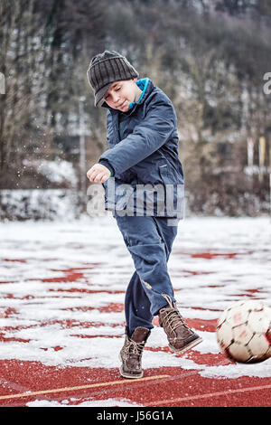 Ragazzo calciare il pallone in inverno sulle lastre di ghiaccio Foto Stock