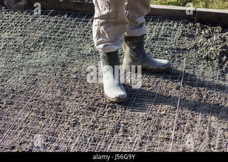 Lavoratore con stivali permanente sulla rete metallica del seminterrato riempito con calcestruzzo fresco Foto Stock