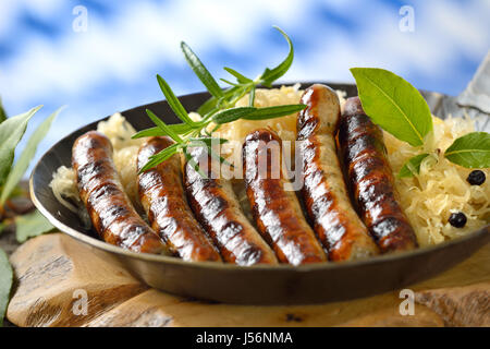 Frittura di salsicce di Norimberga su crauti servita in un ferro da stiro a padella, sullo sfondo la bandiera bavarese Foto Stock