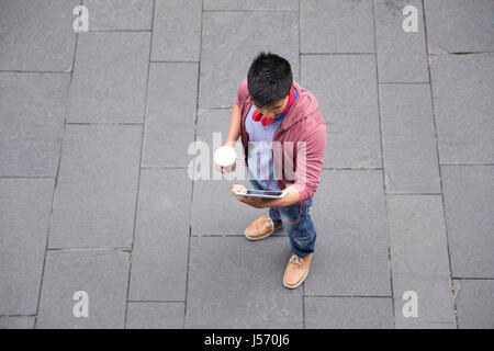 Elevato angolo di visione di un uomo cinese permanente sulla via della città utilizzando un dispositivo tablet pc. Foto Stock