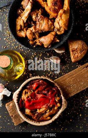 Alta angolazione di una ciotola con lo spagnolo escalibada, un mix di verdure grigliate, una ciotola con arrosti di carne di pollo e coniglio, una ampolla di olio di oliva, alcuni gar Foto Stock