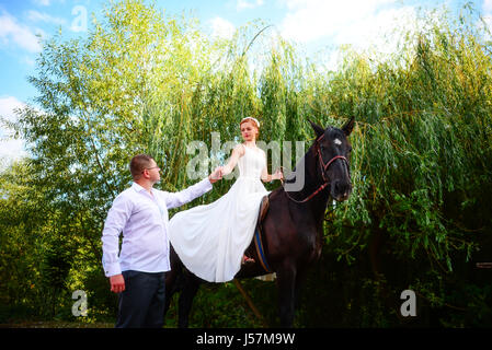 Lo sposo conduce il cavallo per la briglia. Sposa siede in sella a cavallo. Paese wedding Foto Stock