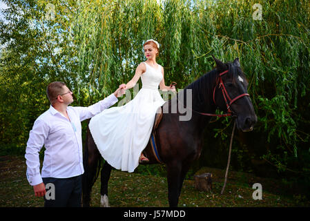 Lo sposo conduce il cavallo per la briglia. Sposa siede in sella a cavallo. Paese wedding Foto Stock