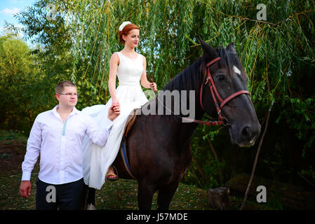 Lo sposo conduce il cavallo per la briglia. Sposa siede in sella a cavallo. Paese wedding Foto Stock