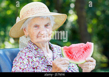 Felice donna anziana mangiando anguria in giardino Foto Stock