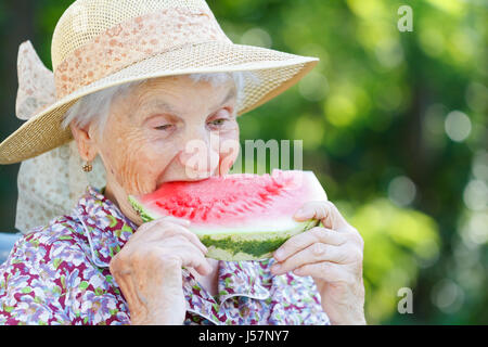 Felice donna anziana mangiando anguria in giardino Foto Stock