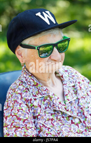 Senior donna che indossa gli occhiali da sole e cappello da baseball Foto Stock