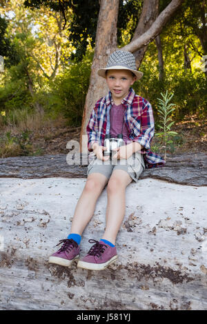 Ritratto di ragazzo seduto su i caduti tronco di albero nella foresta Foto Stock