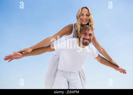 Angolo basso ritratto di uomo felice piggybacking ragazza contro il cielo chiaro Foto Stock