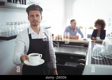 Ritratto di cameriere tenendo una tazza di caffè al contatore nel ristorante Foto Stock