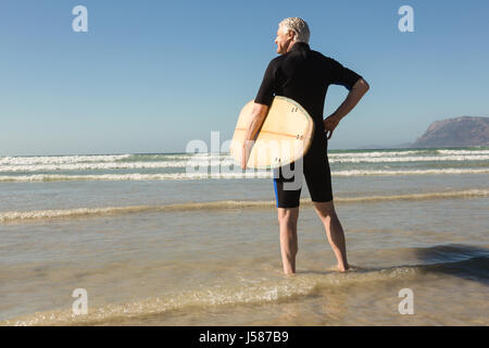 Vista posteriore del senior l uomo nella muta carryig tavole da surf in spiaggia Foto Stock