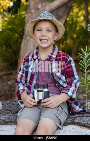 Ritratto di ragazzo seduto su i caduti tronco di albero nella foresta Foto Stock